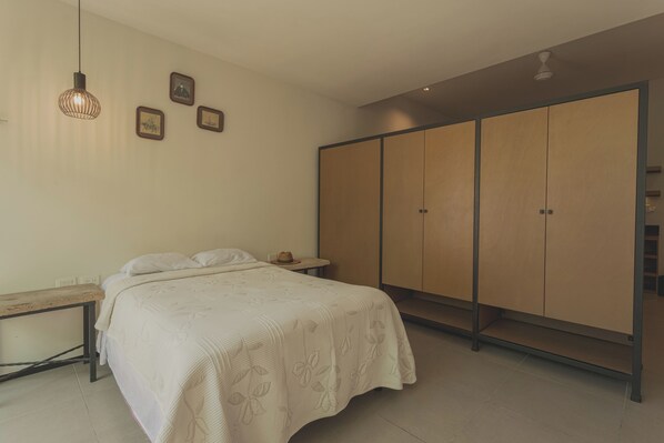 A bedroom with a bed, a wooden bench, a wardrobe, and a hanging light fixture. - Estudio LALO Temozon Norte Mérida (Mérida)