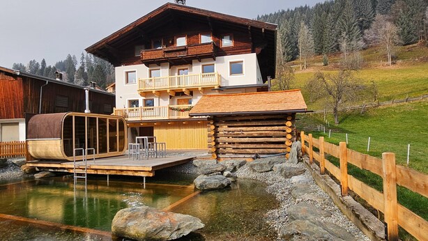 A log cabin with a wooden deck and a small pond. - Farmhouse in Bramberg With Sauna & Ski Access (Bramberg am Wildkogel)