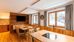 A wooden interior with a dining table, chairs, a TV mounted on a wooden wall, and a window with curtains. - Farmhouse in Bramberg With Sauna & Ski Access (Bramberg am Wildkogel)