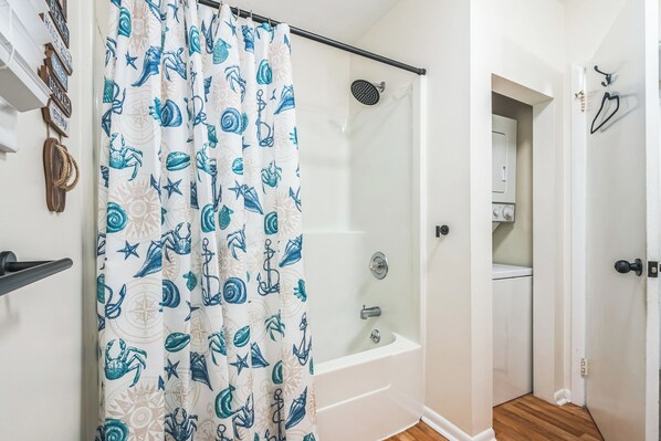 A bathroom with a shower, a bathtub, and a door leading to a laundry area. - Castaway Cottage, A Cozy 2-Bedroom Condo in OCNJ. Pet Friendly (Ocean City)