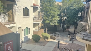 A courtyard with a paved walkway, a small garden area with a fire pit, and a building with a balcony.