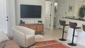 A modern living room with a sofa, a TV, a cabinet, and a kitchen area with bar stools.