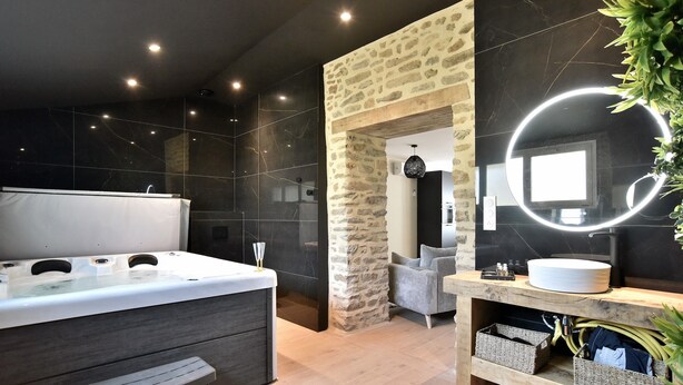 A modern bathroom with a stone archway, a large mirror with a circular light, a bathtub, and a vanity with a sink and storage baskets. - Cocoon Rance - One Bedroom House, Sleeps 2 (Plouër-sur-Rance)
