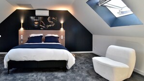 A modern bedroom with a sloped ceiling, a bed with a dark headboard, a white armchair, and a skylight. - Cocoon Rance - One Bedroom House, Sleeps 2 (Plouër-sur-Rance)