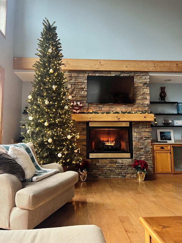 A living room with a fireplace, a Christmas tree, and a flat-screen TV mounted above it.