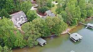 Una casa grande con un muelle y un pequeño embarcadero junto a un lago rodeado de árboles frondosos.