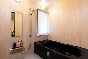 A modern bathroom with a black bathtub, a shower, and a mirror. There are three bottles of toiletries on a shelf. - Rinn Gion Yasaka (Kyoto)
