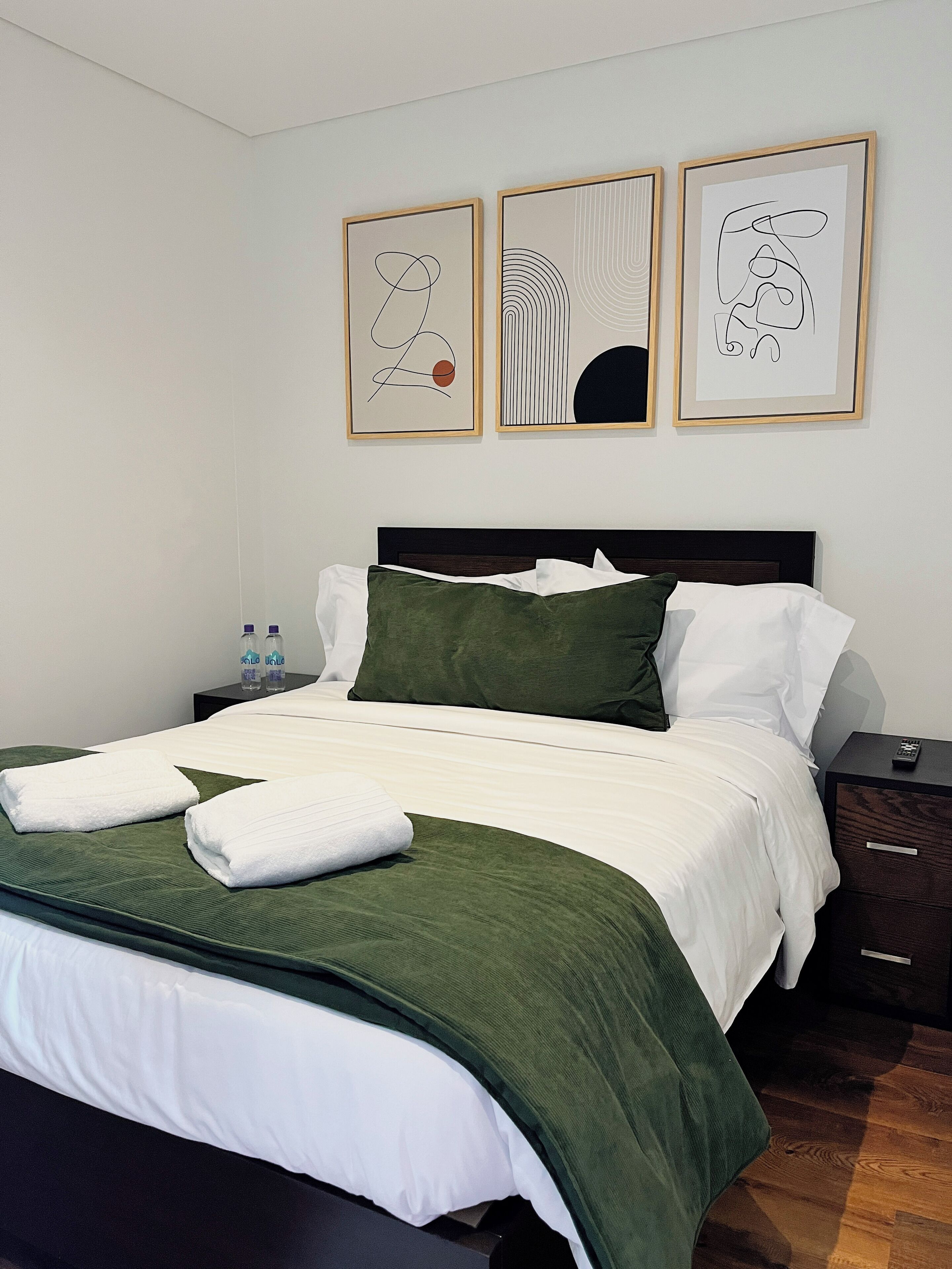 A neatly made bed with green and white bedding, a dark headboard, and a nightstand with a remote control.