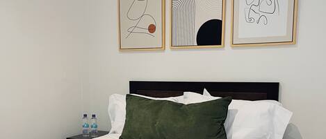 A neatly made bed with green and white bedding, a dark headboard, and a nightstand with a remote control.