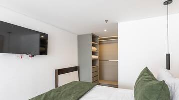A bedroom with a bed, a TV mounted on the wall, a closet with shelves, and a hanging light fixture.