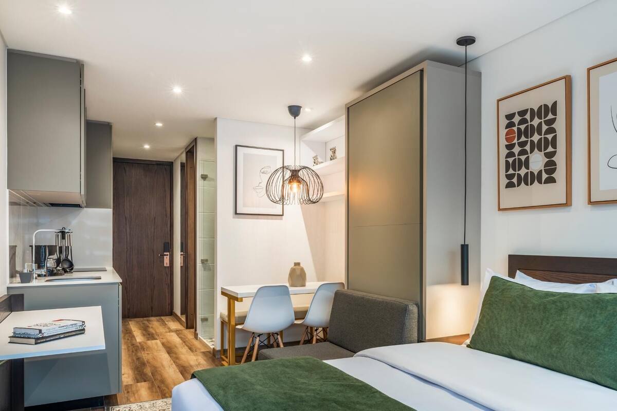 A modern hotel room with a bed, desk, chairs, and a dining area.