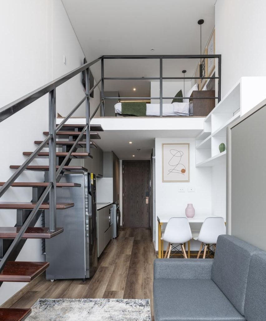 A modern interior with a staircase leading to a loft bedroom, a kitchen area, and a seating area with a sofa and chairs.