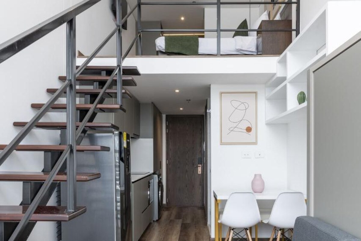A modern interior with a staircase leading to a loft bedroom, a kitchen, and a seating area with a sofa and chairs.