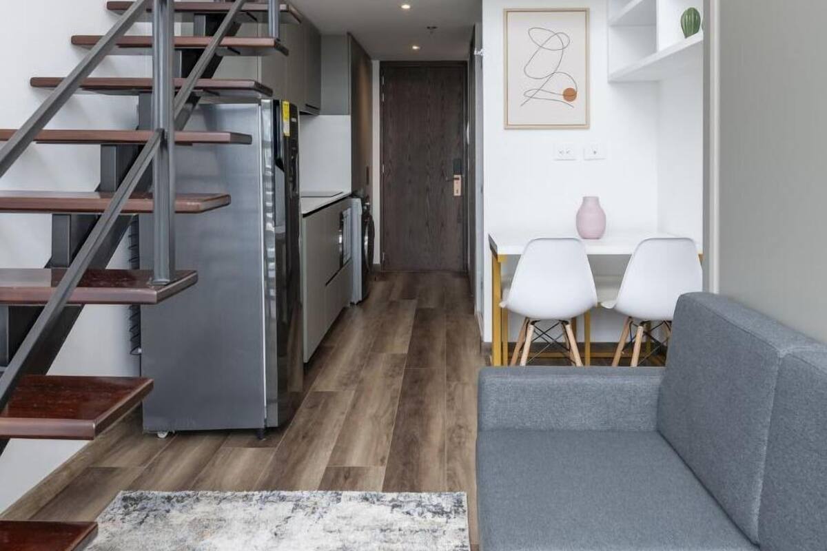 A modern interior with a staircase leading to a loft bedroom, a kitchen, and a seating area with a sofa and chairs.