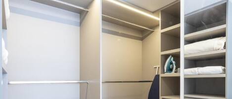 A walk-in closet with open shelving and drawers, a hanging rack, and a visible iron.