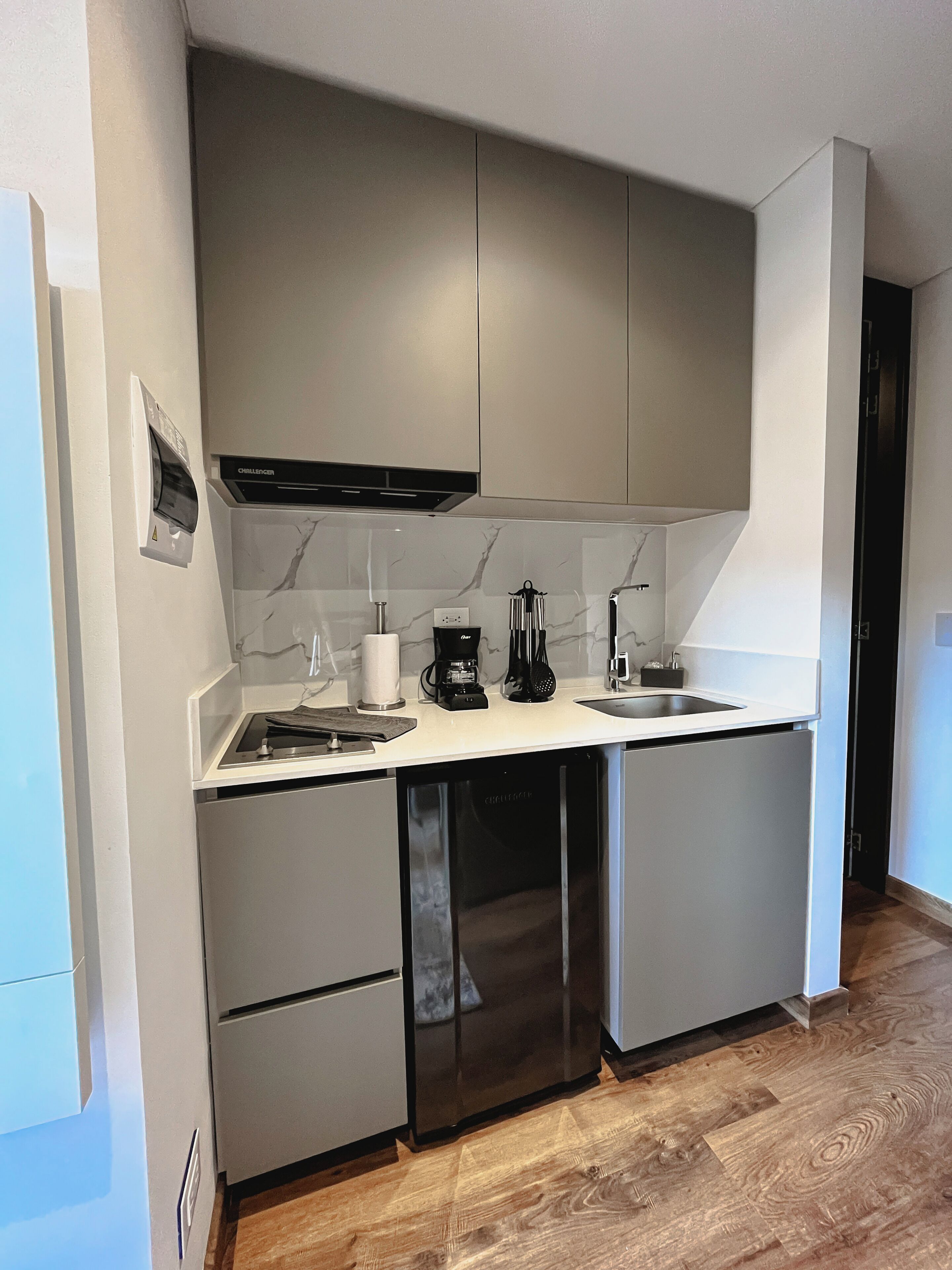 Ett kompakt kök med grå skåp, en inbyggd diskmaskin och en kaffebryggare.