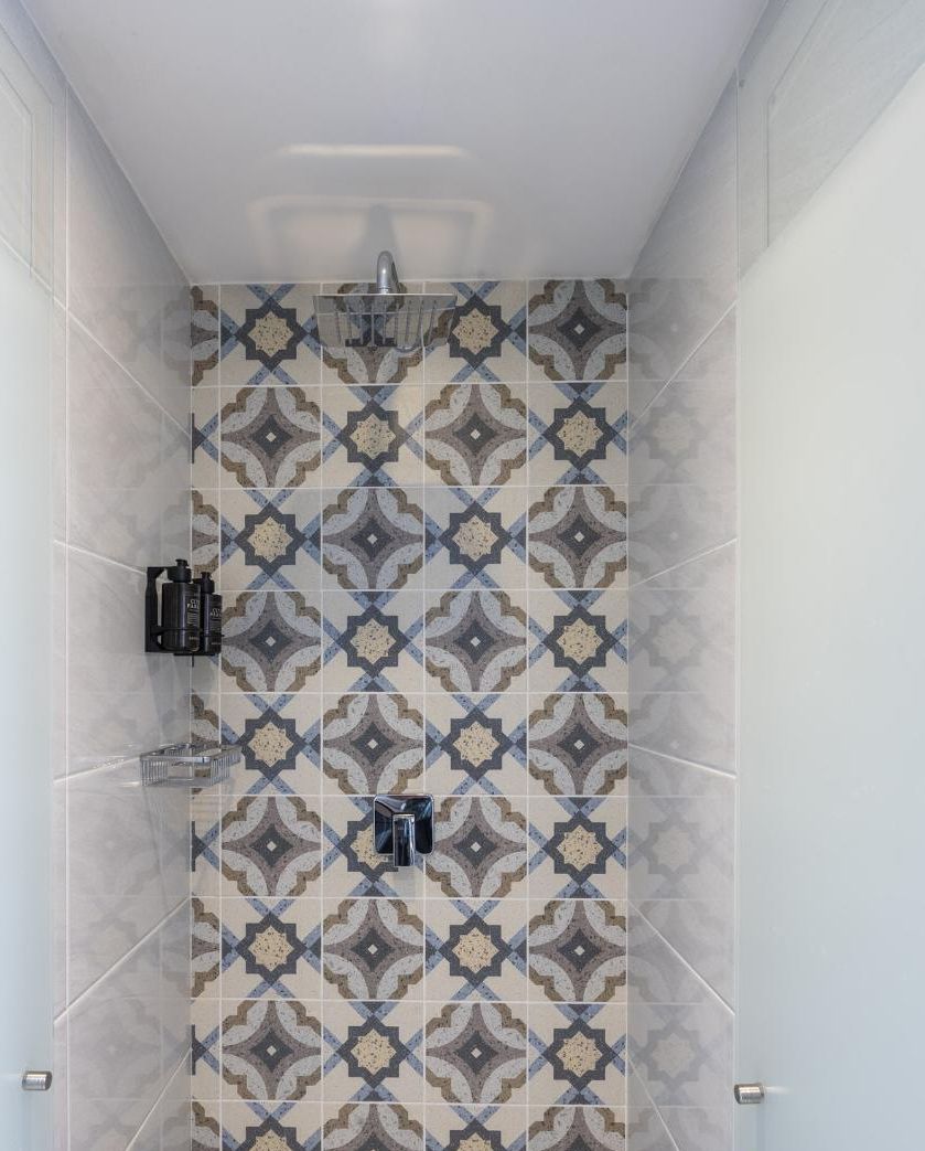 A shower with a patterned tile wall, a handheld showerhead, and a soap dispenser.