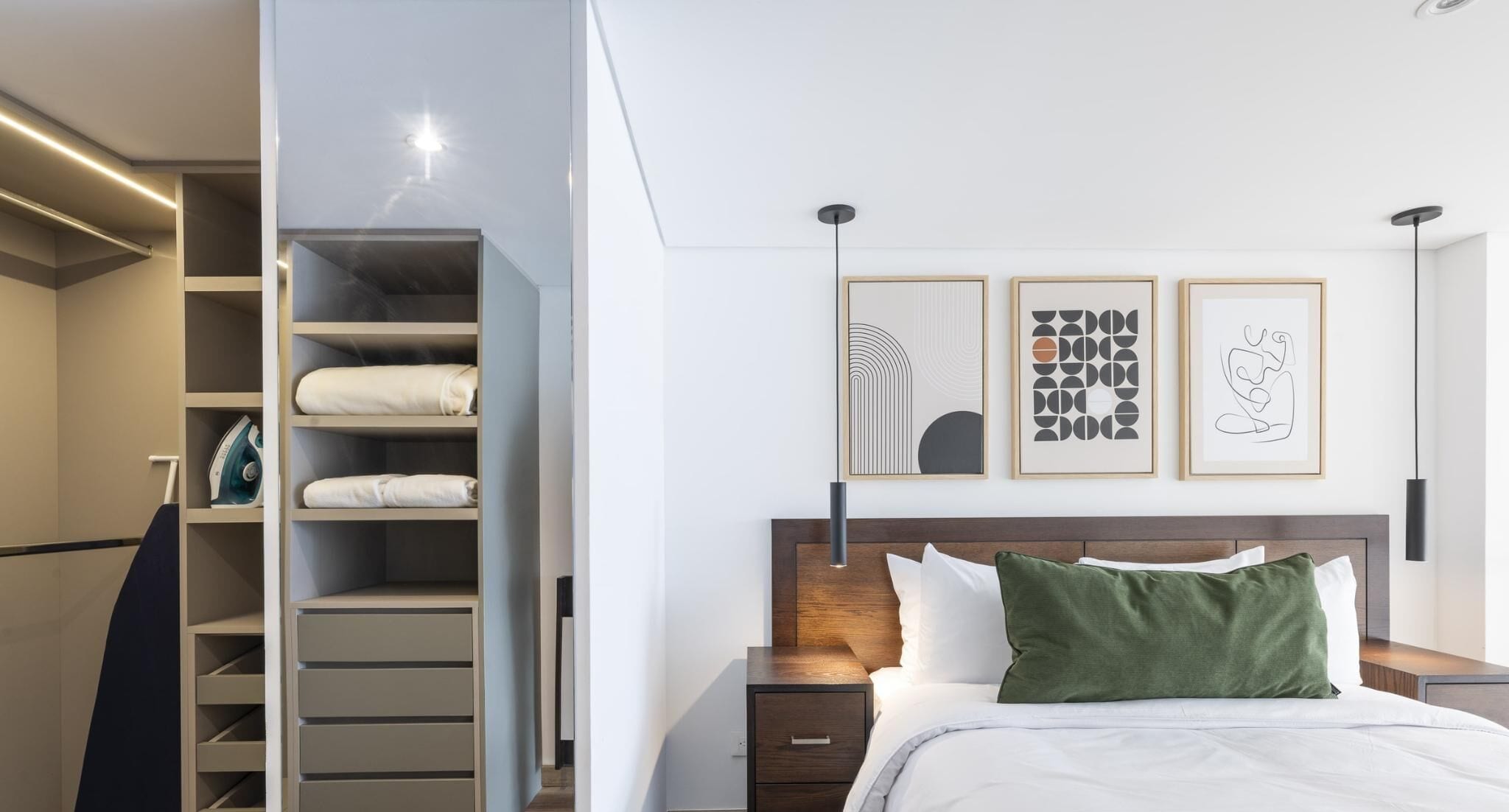 Een moderne slaapkamer met een bed, nachtkastjes, een kledingkast en drie ingekaderde kunstwerken aan de muur.