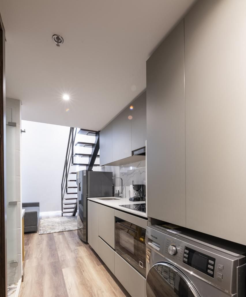 Eine moderne Küche mit integrierten Geräten, einer Treppe, die in ein Obergeschoss führt, und einer sichtbaren Waschmaschine.
