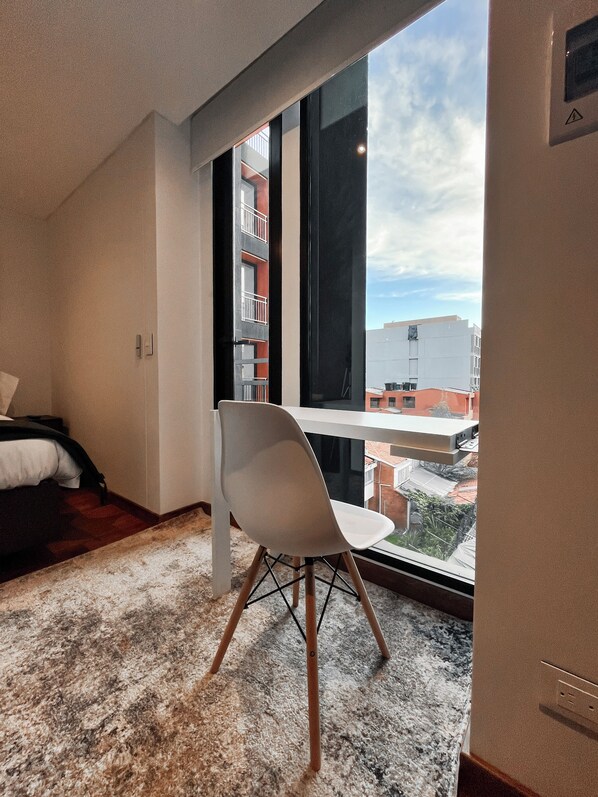 A modern hotel room with a large window, a white chair, a bed, and a carpeted floor. - Edificio Taj 97 By Jalo (Bogotá)