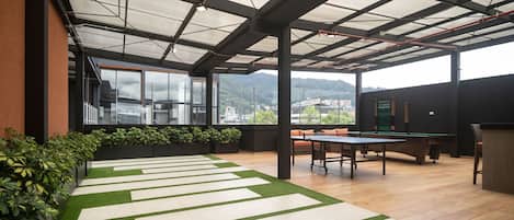 A modern indoor space with a ping pong table, a pool table, and a seating area with a view of the city and hills.
