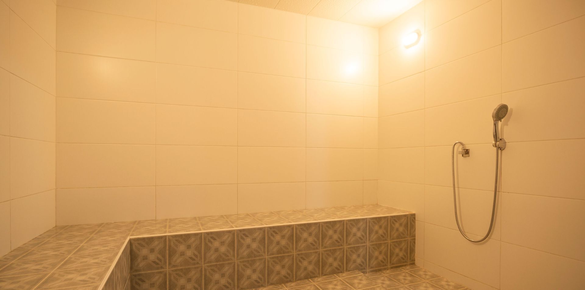 Un baño pequeño con azulejos, un banco y un cabezal de ducha manual.