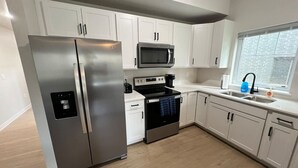 Una cocina moderna con armarios blancos, electrodomésticos de acero inoxidable y un ventanal que proporciona luz natural.