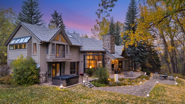 Une maison à deux étages avec une façade en pierre, une grande terrasse et un patio couvert.