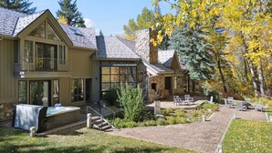 Une maison à deux étages avec une cheminée en pierre, un espace salon extérieur et un jacuzzi.