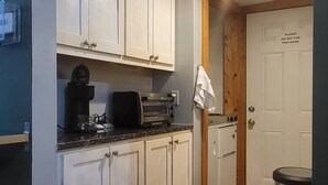 A kitchen with white cabinets, a countertop with a coffee maker, toaster, and kettle, a wooden floor, and a trash can. - Charming house with WiFi and AC in superb Randolph (Randolph)