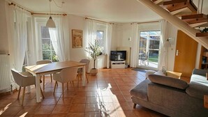 A spacious living area with a dining table, chairs, a sofa, a TV, and a staircase. - Haus in Nessmersiel am Wattenmeer (Dornum)