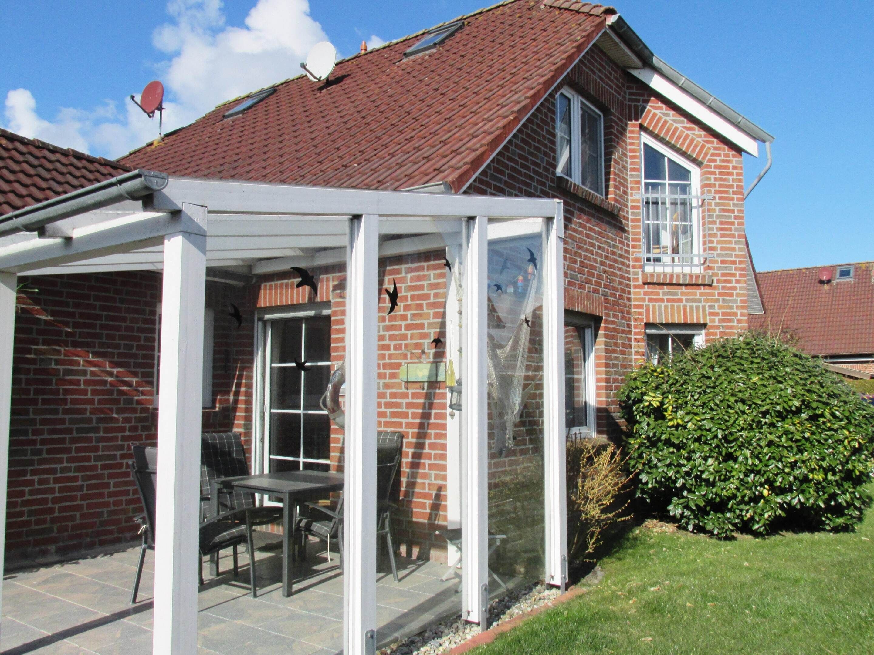 A house with a brick exterior, a red-tiled roof, and a glass-enclosed patio with a table and chairs.