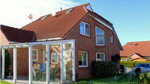 A two-story brick house with a red-tiled roof, a glass conservatory, and a white picket fence. - Haus in Nessmersiel am Wattenmeer (Dornum)