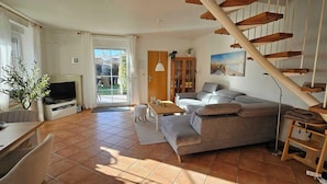 A living room with a sofa, TV, and a staircase. - Haus in Nessmersiel am Wattenmeer (Dornum)