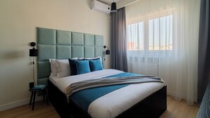 A modern hotel room with a large bed, a headboard, a bedside table, a lamp, and a window with curtains. - Faculty of Law Studios (Bucharest)