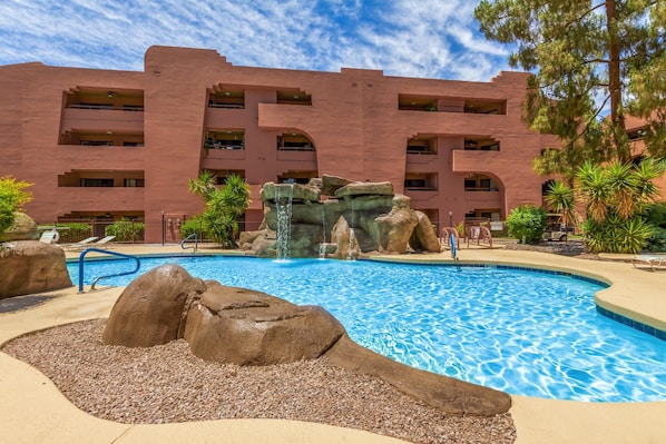 A hotel with a swimming pool surrounded by large rocks and pebbles.