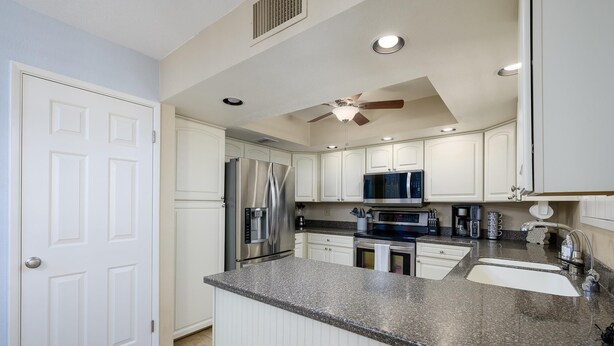 A modern kitchen with white cabinetry, a granite countertop, stainless steel appliances, and a ceiling fan. - Casa Rosa-4th Floor Gorgeous Condo (Phoenix, Arizona)