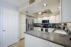 A modern kitchen with white cabinetry, a granite countertop, stainless steel appliances, and a ceiling fan.