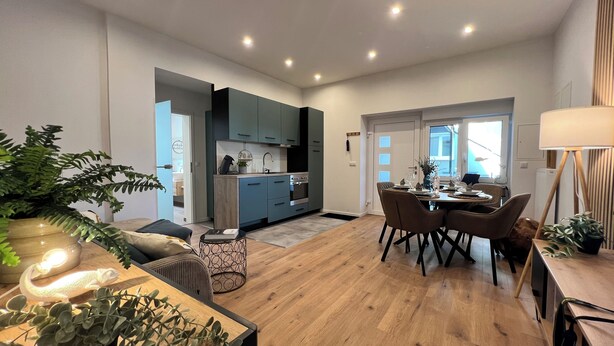 Una cocina moderna con armarios azules, un comedor con mesa y sillas de madera, y una sala de estar con sofá y mesa de centro.