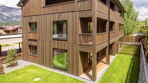 A multi-story wooden building with balconies, large windows, and a well-maintained lawn. - Premium Holiday Apartment With Sauna and Garden (Haus)