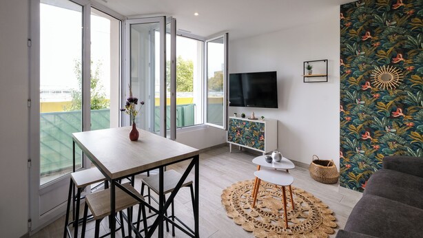Una sala de estar moderna con una mesa de comedor de madera, un sofá, un televisor montado en la pared y un balcón con vista a la ciudad.