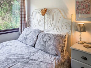 Un lit avec une couvre-lit à motifs, une tête de lit décorative, une lampe de chevet et une table de chevet avec des tiroirs.