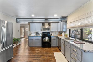 Une cuisine moderne avec des meubles gris, des appareils électroménagers en acier inoxydable et un plancher en bois.