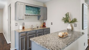 Une cuisine dotée de plans de travail en granit, de meubles gris et d’un pare-feu orné d’un motif de marbre bleu.