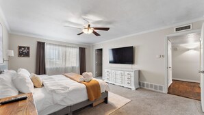 Une chambre d’hôtel avec un lit, une télévision, un ventilateur de plafond, une commode et une porte.
