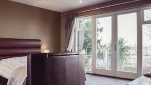 Un dormitorio con una cama grande, una mesita de noche y vistas al exterior a través de un ventanal corredero.