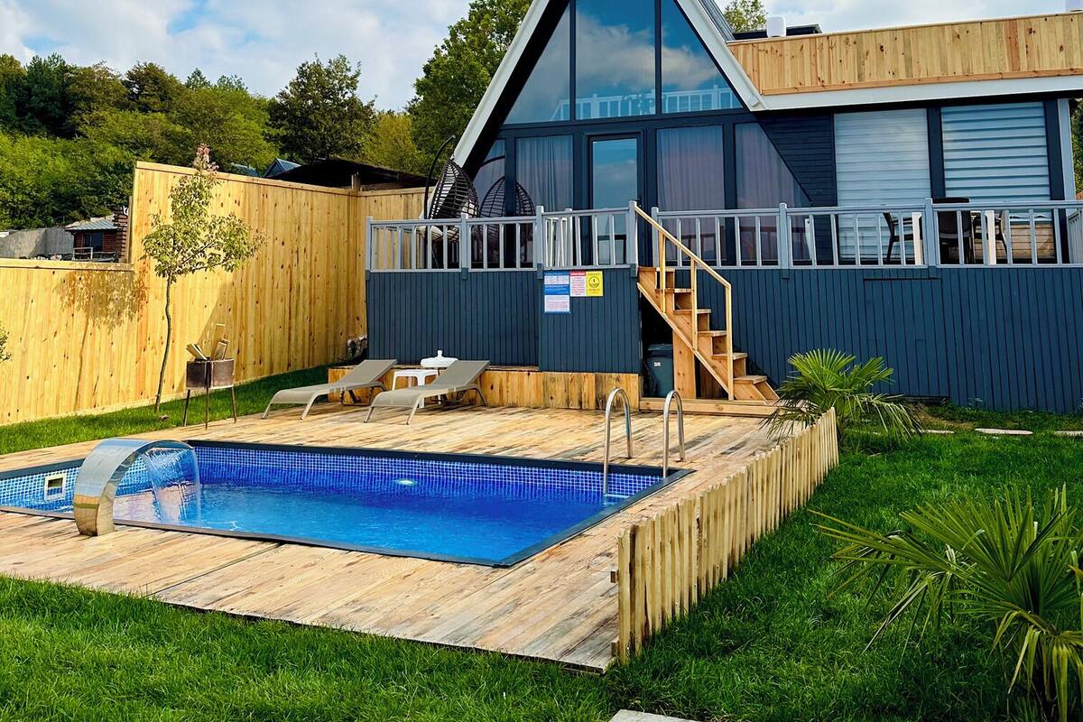 A modern house with a swimming pool, a wooden deck, and a staircase leading to a balcony.