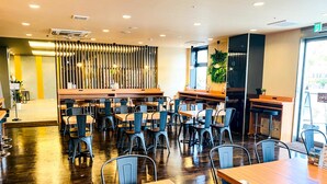 Ein modernes Restaurantambiente mit Holztischen und -stühlen, einer zentralen Bar und einer dekorativen Wandverkleidung.