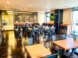 A modern restaurant interior with wooden tables and chairs, a central bar area, and a decorative vertical panel. - Hotel Livemax Premium Nagano Ekimae (Nagano)