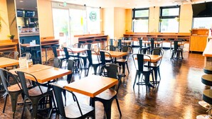 Ein geräumiges Restaurant mit Holztischen und -stühlen, einer Theke mit Speisekarte und großen Fenstern, die viel Tageslicht hereinlassen.